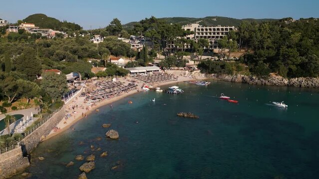 Drone ascends above water to showcase boat leaving dock as tourists play and relax in Corfu Greece