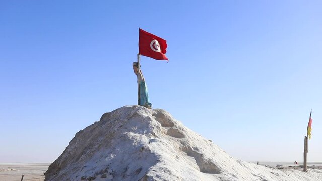 Statue holding Tunisian flag atop salt hill in Chott el Jerid desert under clear sky