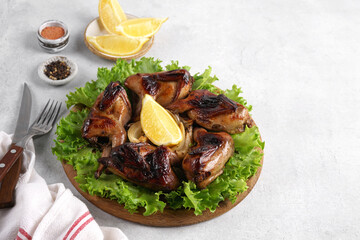 Oven baked quails with onions, spices and herbs in a wooden plate with greens. Gray background. copy space