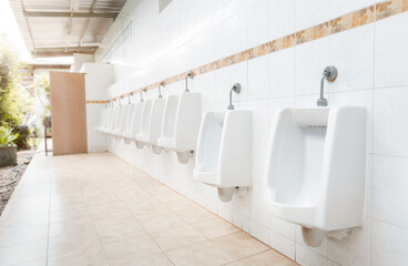 Men's room with white porcelain urinals in line. Modern clean public toilets with tiles . Comfort...