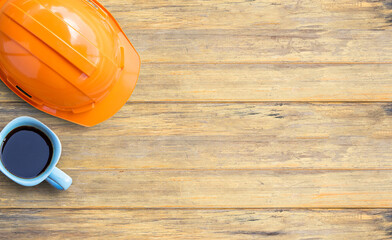 Top view with orange safety helmet and cup of coffee on old wooden table