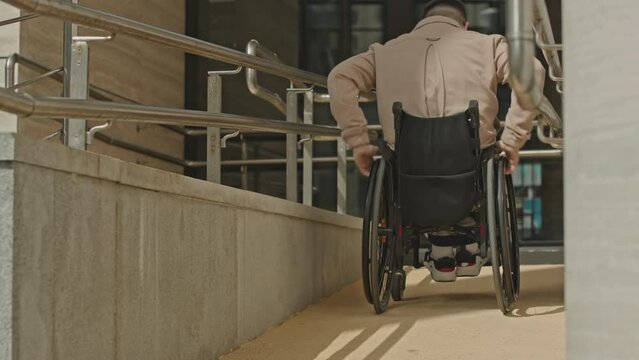 Man riding wheelchair on ramp in front of office building during day in city