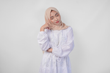 Fototapeta premium Thoughtful young Asian Muslim woman wearing white dress and hijab, holding her chin and thinking with serious expression over isolated white background