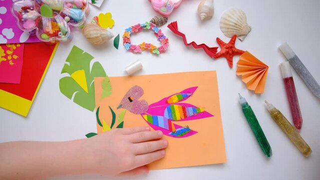 Child making homemade greeting card, applique with bird, hummingbird or colibri and flowers from pieces of paper, tropical garden. Gift for Mothers day, Birthday, Easter, holidays.