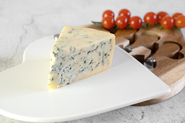Soft cheese with blue and white mold on a white board. A slice of dor bleu cheese on a special cheese board with special cheese knives