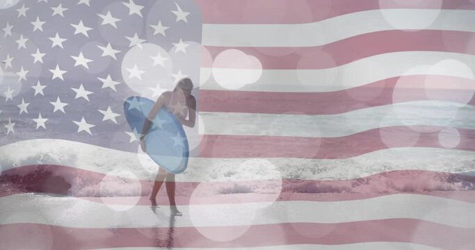 Animation of american flag and light spots over caucasian woman carrying surfboard on sunny beach