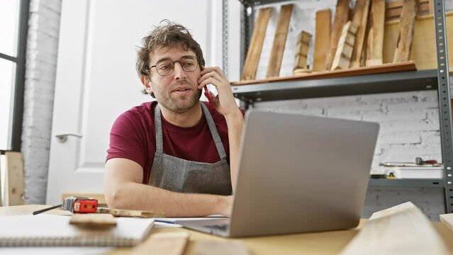 Carpenter multitasks between a phone call and laptop in a workshop setting, conveying a vibe of modern craftsmanship.