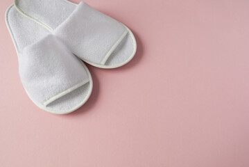 White slippers on pink background. Slippers for a hotel. Flat layer, top view.