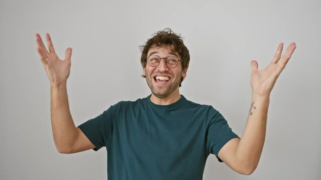 Triumphant young hispanic man with glasses bursts with joy, celebrating a thrilling win! he raises his hands victoriously, standing on a white isolated background, beaming that winner smile.