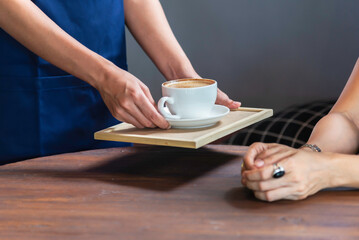 Waitress with apron serving iced coffee to customer at cafe.