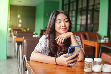 Daydreaming young Asian woman wearing dress sitting at a restaurant for a breakfast, holding a...