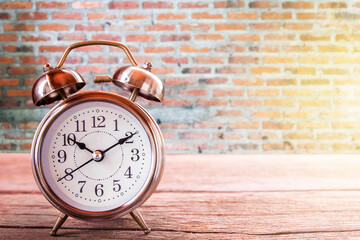 Retro alarm clock on a wooden table with blurred brick wall background.