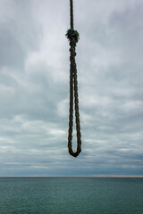 A sturdy rope loop hangs against a serene ocean horizon. The sky and the sea merge in a peaceful...
