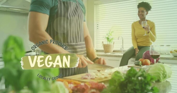 Animation of vegan text over diverse couple preparing healthy meal in kitchen