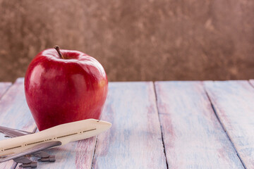 Close up red apple and toy airplane on wooden background.