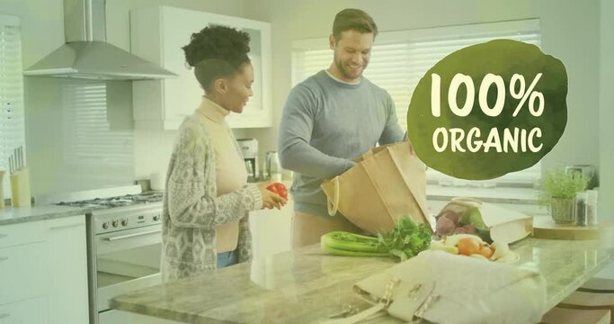 Animation of 100 percent organic text over diverse couple preparing healthy meal in kitchen