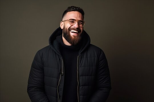 Handsome bearded man in a black jacket and glasses on a dark background.