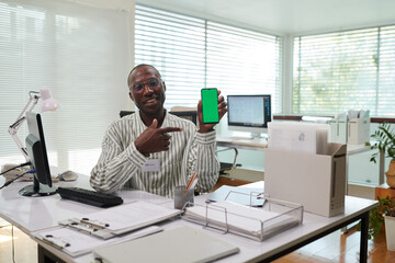 Portrait of positive Black office manager showing banking application on smartphone, green screen