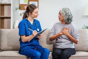 Fototapeta premium Caucasian teenager female doctor consults with and Asian elderly patient on medical history, discussing headaches, chest pain, coughing, sneezing, stomach pain, and neck pain while seated on a sofa.