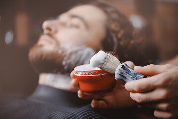 Closeup barber shaving man with sharp steel razor, barbershop warm retro old toning