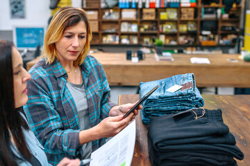 Portrait of blonde woman holding digital tablet next to her partner while checking clothes stock on...