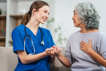 Caucasian female doctor offers encouragement to Asian mature elderly patient woman while holding hands, providing comfort and support during a medical consultation at sofa.