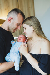 Happy young parents holding their newborn baby in their arms. Romper on a newborn boy. Newborn baby in the hands of mom and dad