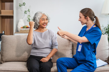Caucasian female doctor shares a celebratory high five with an elderly Asian patient while both are...