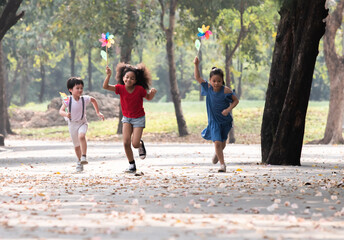 Joyful diversity of children sprinting in a park, with windmills in hands, laughing happiness on sunny day, young school kids' friends enjoy outdoor activities running and playing together on weekend