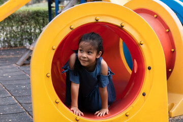 Kid playing in playground, Joyous child emerges from a colorful playground tunnel, smile girl enjoy the playful hues surrounding her, happy young girl playing alone exits play tube, moment of fun