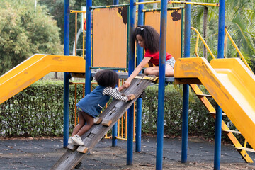 Diversity children adopted playing in playground, Joyous kids appear from playground tunnel, sibling girls enjoy in park surrounding her, happy young girl playing emerge from play tube, moment of fun