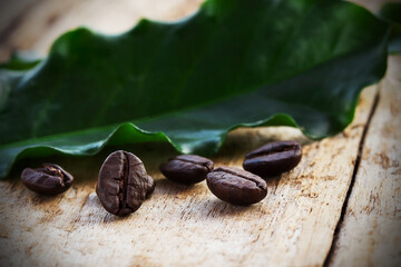 Coffee beans and green leaf on wooden background
