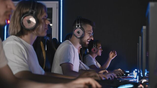 Team of gamers playing video game on PC at computer club, cyber sport tournament. E-sport championship. 5 players in headset communicate with each other over mic. Multiplayer online competition