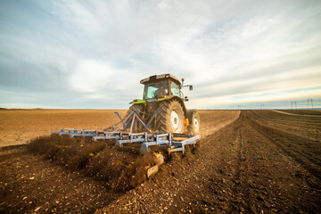 Wide-angle view of a tractor plowing farmland against a dramatic sunset sky