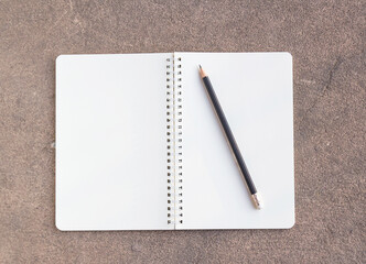 Blank paper notebook and pencil on cement floor background. Top view with copy space (selective focus).