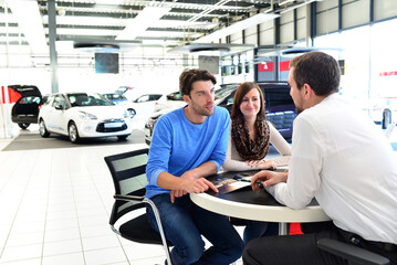 young couple buying a new car in the showroom of a car dealership - signature sales contract with...