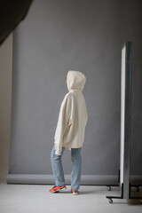 Beautiful blonde woman in a white hoodie and blue jeans posing on a gray background