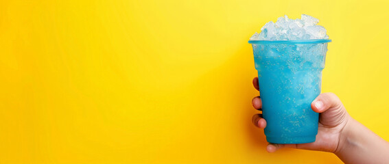 The hand holds a cup with a milk slushie. A  blue glass with a  coconut slushie  on a yellow background, place for text