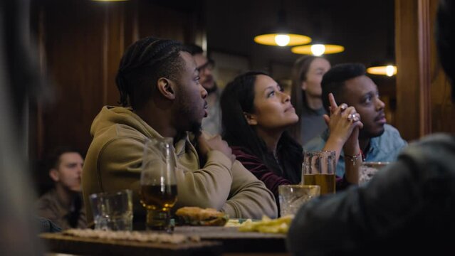 Happy sport fans celebrating and cheering when football team scores goal and wins world league championship. Group of multicultural people applaud and shout watching soccer match live in bar or pub.