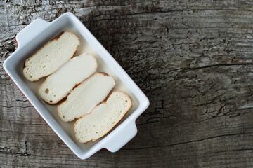 Slices of bread soaking in milk to make torrijas. Rustic wooden background. Copy space.
