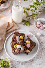 Chocolate brownie with Easter candies in the form of colored eggs with a bottle of milk. Easter dessert. Copy space.