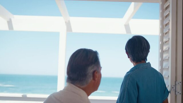 Mature couple on holiday in beach front property overlooking ocean with man kneeling and proposing marriage to woman with ring which she accepts - shot in slow motion