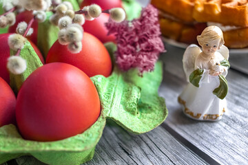 Red Easter eggs in box, figure of an angel with dove in his hands, willow branches on wooden table. close-up. Christian symbols and holidays. Spring time