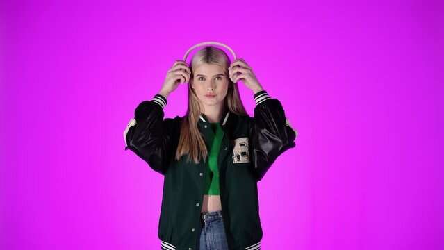 Blonde woman puts on over ear headphones, isolated purple background, studio