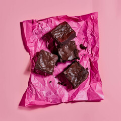 Chocolate brownies lying on light pink paper and pink background. Bold colors. Modern food photography.