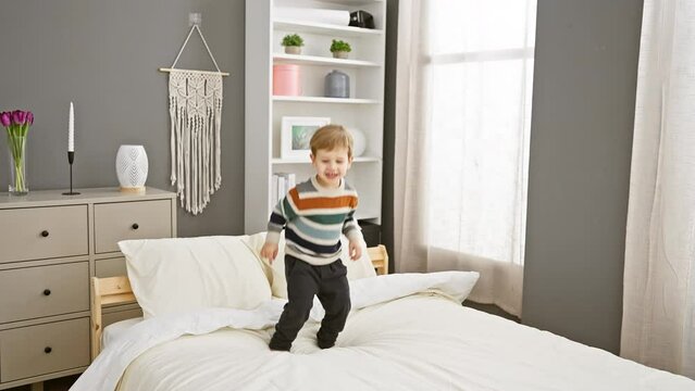 A joyful toddler boy plays on a bed in a cozy home bedroom, depicting carefree childhood moments indoors.