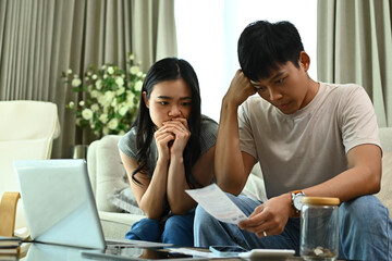 Unhappy young couple calculating family spends together and feeling depressed.