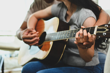 Fototapeta na wymiar Cropped shot of young couple couple singing a song and playing guitar on sofa in living room