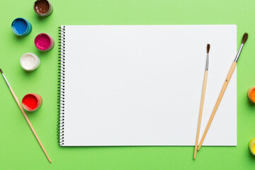 Album pages and paints, pencils, brush on a colored background. Top view with empty space. workplace for creativity. home teaching concept drawing