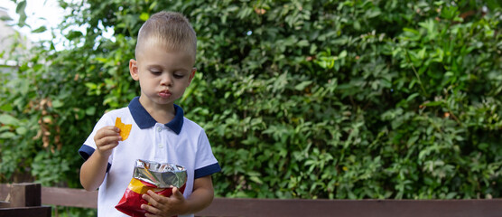 a child eats chips from a pack on the background of nature